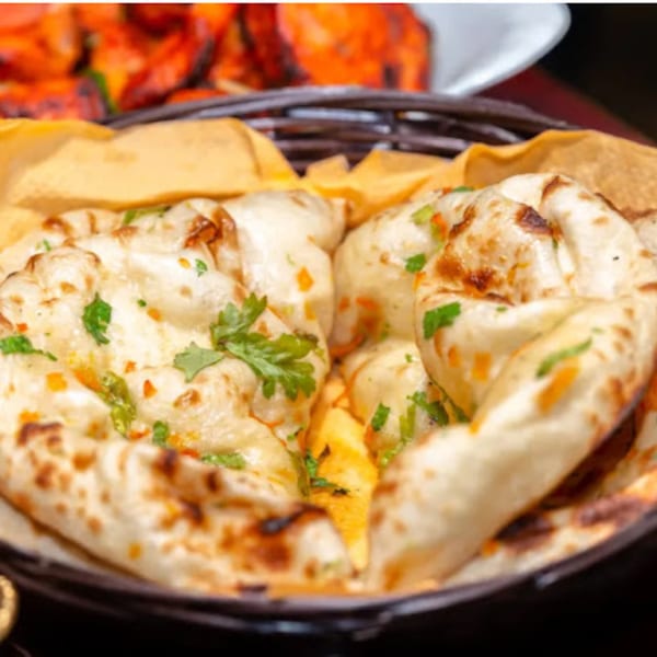 Basket of freshly baked naan bread, garnished with cilantro and spices, from Sherpa Indian Kitchen.