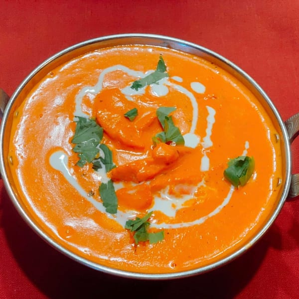 Sherpa Indian Kitchen's vibrant orange butter chicken, garnished with cream swirls and fresh cilantro, in a metal bowl.