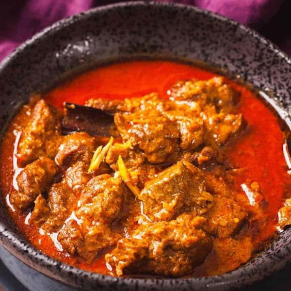 Close-up of Sherpa Indian Kitchen's vibrant red Indian curry with tender meat pieces and ginger garnish.
