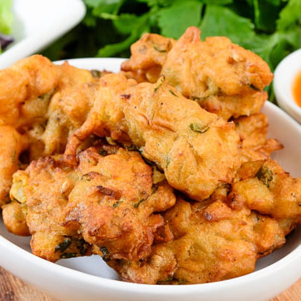 A white bowl filled with golden-brown, crispy Indian pakoras, garnished with green herbs.