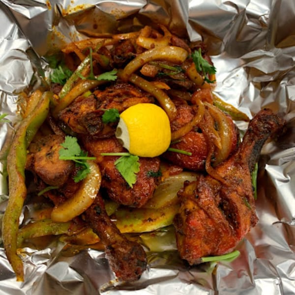 Indian chicken dish with onions, green peppers, and a lemon wedge, served in foil.